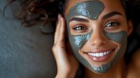 Young African American woman with bright smile wearing gray clay face mask during skincare routine, wellness and beauty treatment at home spa session.