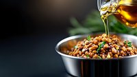 Golden oil drizzling over warm lentil salad with fresh herbs in metal bowl against dark background, food photography highlighting texture and appetizing details.