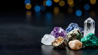 Collection of healing crystals and gemstones including amethyst, quartz, malachite and pyrite arranged on dark surface with bokeh lights background.