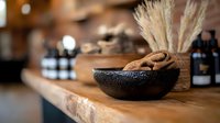 Natural spa wellness setup with volcanic stone bowl containing organic nuts on wooden counter with essential oil bottles and dried pampas grass for relaxation.