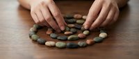 Hands arranging colorful smooth river stones in spiral pattern on wooden surface for meditation, mindfulness practice, zen garden design, and holistic wellness.