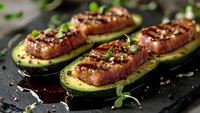 Grilled avocado halves stuffed with seasoned sausages, topped with herbs and nuts on dark slate surface for healthy cooking and meal preparation.