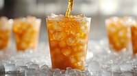 Golden liquid pours into clear glass filled with ice cubes creating refreshing cold drink splash, backlit with soft bokeh background and scattered ice.
