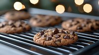 Freshly baked chocolate chip cookies cooling on metal rack with soft bokeh lights in background, close-up view showing melted chips and golden brown texture.