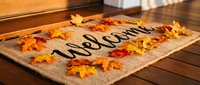 Welcome doormat decorated with colorful autumn maple leaves on a wooden porch, creating a warm and inviting seasonal home entrance atmosphere.