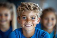 Happy blonde boy with blue eyes smiling at camera in classroom setting with classmates in background for educational and childhood concepts.