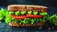 Fresh vegetarian sandwich with whole grain bread, sliced avocado, juicy tomatoes and crisp lettuce on dark background, healthy lunch option.