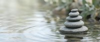 Zen stone stack balanced on water surface creating peaceful meditation scene with soft natural lighting and blurred background for wellness concepts.