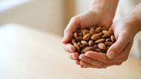 Hands holding handful of almonds, raw nuts in palms for healthy snacking, nutrition and wellness content.