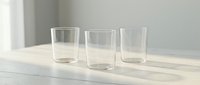 Three empty clear glass tumblers arranged on white wooden surface with soft natural lighting and minimalist aesthetic for kitchen and dining concepts.