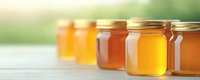 Glass jars filled with different varieties of golden and amber honey arranged in row on wooden surface against soft blurred natural background. Fresh organic sweetener.