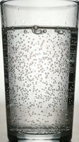 Sparkling water in a clear glass with rising carbonation bubbles, close-up macro shot for healthy lifestyle and beverage concepts.