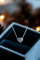 Elegant silver heart pendant necklace in jewelry box with soft bokeh lights creating romantic atmosphere, perfect for Valentine's Day or anniversary gift promotion.