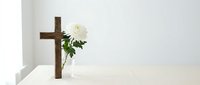 Wooden cross with white rose on clean table against minimalist white background for memorial, funeral, religious ceremony or spiritual remembrance concept.