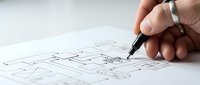 Hand drawing architectural floor plan with black pen on white paper showing detailed room layouts and measurements for construction project.