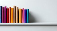 Colorful book spines arranged in rainbow order on white shelf against neutral wall, creating minimalist composition for education and learning concepts.
