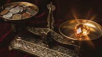 Vintage brass balance scale with ornate decorations weighing coins against gemstone in warm golden light creating dramatic shadows on dark background.