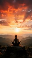 Woman meditating in lotus pose on mountain peak at sunset with dramatic orange clouds and layered hills creating peaceful spiritual atmosphere.