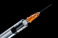 Medical syringe with orange liquid medication against black background, close-up view showing needle and transparent barrel for healthcare concepts.