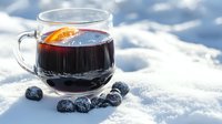 Glass cup of mulled wine garnished with orange slice and scattered blueberries on fresh snow background, winter holiday drink in natural setting.