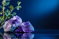 Purple amethyst crystal cluster with green plant on reflective surface against deep blue background for healing meditation and wellness concepts.