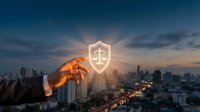 Professional businessman hand reaching toward glowing justice scale shield icon over city skyline at sunset for legal protection and security services.