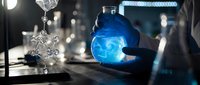 Scientist in protective gloves holding glowing blue chemical solution in laboratory flask during research experiment with molecular structures and equipment.