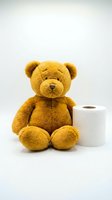 Cute brown teddy bear sitting next to toilet paper roll on white background, potty training concept for toddlers and children bathroom education.