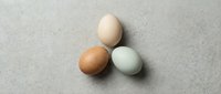 Three fresh farm eggs in natural colors arranged on textured concrete surface for cooking and baking projects.
