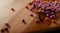 Scattered pink and orange medical pills and capsules on wooden surface with dramatic lighting and shallow depth of field creating pharmaceutical composition.