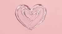 Clear lip gloss heart shape on pink background for cosmetic beauty and skincare product design concepts.