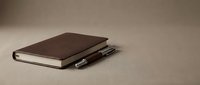Closed brown leather notebook with pen on neutral beige surface, suitable for business, education, and stationery design projects.