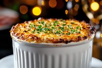 Creamy French onion soup topped with melted gruyere cheese and fresh herbs in white ramekin against festive bokeh lights background. Perfect for restaurant menus.