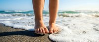 Barefoot person standing in shallow ocean waves on sandy beach at sunrise, relaxation and summer vacation concept.