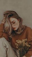 Young blonde woman in cozy brown sweater holding dried flowers with peaceful expression and soft natural lighting for lifestyle content.
