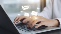 Close-up of female hands typing on laptop keyboard with glowing email icons floating above, representing digital communication and online messaging.