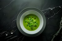 Green pea soup garnished with fresh microgreens served in white bowl on black marble background, dramatic moody food photography styling.