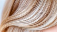 Smooth flowing blonde hair strands with highlights creating soft waves and texture, close-up macro shot showing natural shine and movement on neutral background.