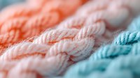 Soft knitted fabric in pastel coral, pink and mint colors showing detailed cable stitch pattern texture. Close up macro photography with selective focus.