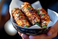 Grilled chicken wings glazed with spicy sauce and garnished with fresh herbs served in decorative bowl with paper liner, close-up shot showing texture and char marks.