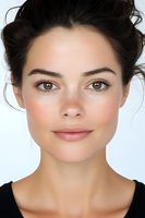 Close up portrait of young woman with natural makeup, brown eyes, and dark hair against white background, showing gentle smile and fresh complexion.