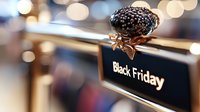 Decorative black glitter bauble with golden bow on retail display sign with blurred bokeh lights background, seasonal shopping concept.