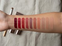 Lipstick swatches on woman's arm showing color palette from deep burgundy to nude shades for makeup testing and cosmetic product comparison.