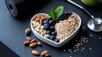 Heart shaped bowl with healthy breakfast ingredients - oatmeal, blueberries, almonds, chia seeds and mint leaf on dark background. Clean eating concept.