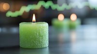 Glowing green frosted candle with soft flame against dark background creates peaceful ambiance, with blurred bokeh lights and reflective surface.
