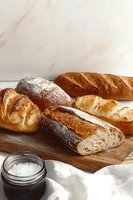 Fresh artisanal bread loaves on wooden cutting board with salt in glass jar, showing crusty exterior and airy crumb texture. Rustic food photography setup.