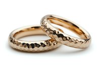 Pair of rose gold wedding bands with hammered faceted surface texture on white background, luxury jewelry photography for bridal and engagement concepts.