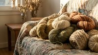 Cozy collection of natural yarn skeins in warm earth tones arranged on vintage armchair for knitting and crochet projects in sunlit room.