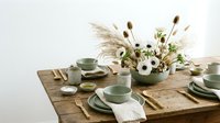 Elegant sage green ceramic dinnerware set arranged on rustic wooden table with dried pampas grass and white flowers for modern dining and home decor styling.