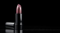 Metallic rose gold lipstick in black tube isolated on dark background with reflection, luxury cosmetic product photography for beauty and makeup advertising.